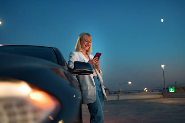 街の通りで車の近くに立っている携帯電話でテキストを横に見ている若い美しい女性 - car smart phone business businesswoman ストックフォトと画像