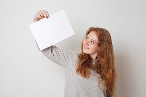 Cute woman looking at empty white paper board against white studio wall banner background