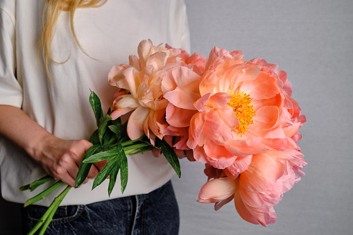 Happy woman holding pink peonies in her hands. The florist girl collected a bouquet of peonies. Delicate flowers are beautiful. A gift for the holiday, spring mood. Romantic surprise