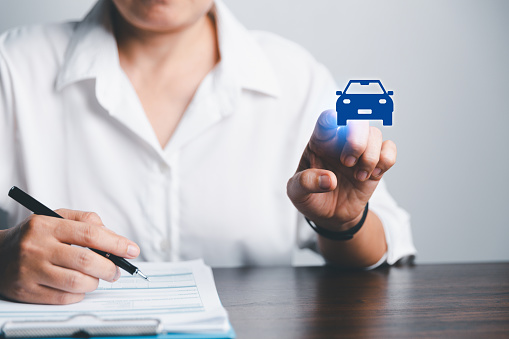 Business woman's hand protecting blue icon car on desk. Planning to manage transportation finance costs. Concept of car insurance business, saving buy - sale with tax and loan for new car.
