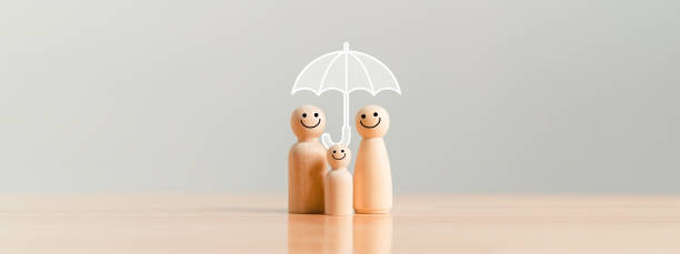 Happy family under the umbrella on raining wooden figurine model on table top background. People lifestyles and Relationships in love concept. stock photo