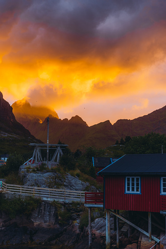 Dramatic view of the bright colorful sky above the mountains and the old fisherman village Å with red houses and reflection sea during the Midnight Sun on Lofoten, Northern Norway