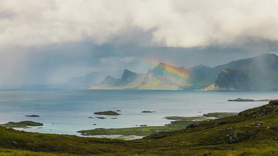 Scenic panoramic view of summer green mountain hills with background view of islands and rainbow after rain in Northern Norway