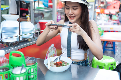 Young adult asian foodie woman backpack traveller eating asia dessert at chinatown street food. travel girls are enjoying with beautiful place in bangkok,