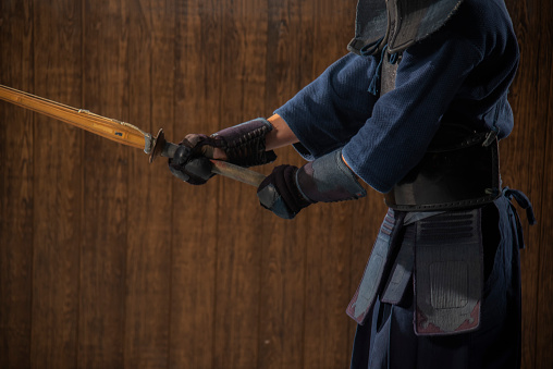 Portrait of man kendo fighter with bokuto Kendo gloves, helmet and bamboo sword on a wooden surface. Kendo armor.