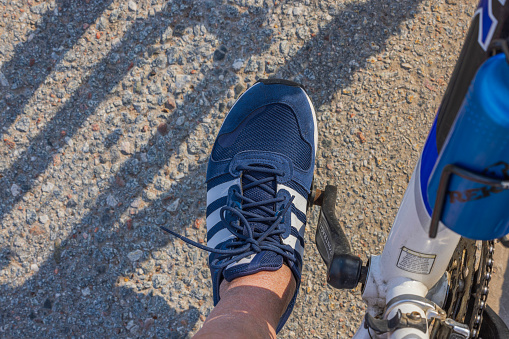 Sweden. Uppsala. 05.14.2023. Close-up view of man's foot in adidas sneakers on bicycle pedal.