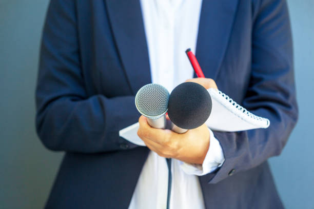 istock Journalist at media event or news conference, holding microphone, writing notes. Broadcast journalism concept. 1494039956