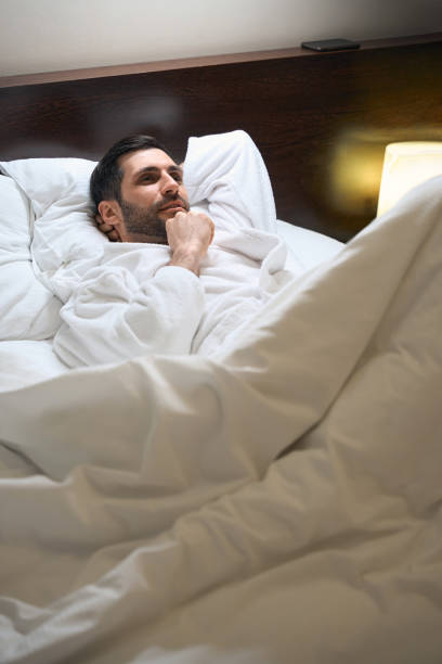 istock Man is resting in bed on soft pillows in hotel room 1494042518