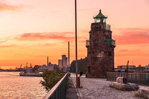 Beautiful summer sunset over a historic stone lighthouse at the end of a cobblestone pier on a river harbor. Bremen, Germany.