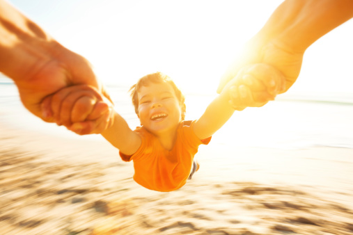 Happy boy spinning around his father on a beach. Motion blur.