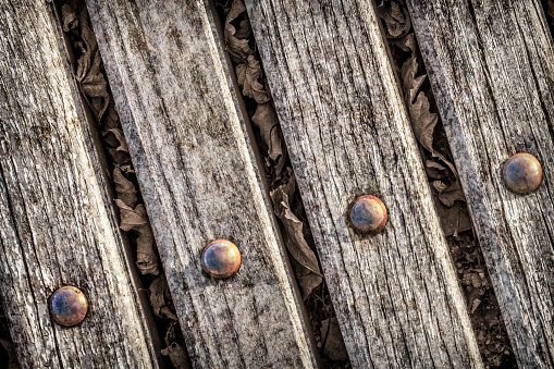 Old, weathered, rotten, cracked, wooden bench slats, fixed with eroded rusty carriage bolts, viewed directly above, vignette background.