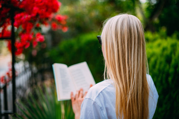 A woman in a red sweater is reading a book. She has long hair and is looking at the pages of the book