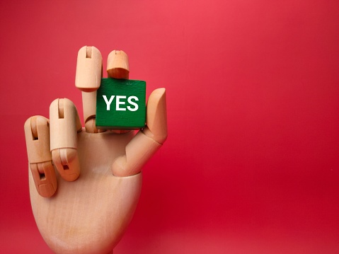 A miniature wooden block with the word 'Yes' inscribed in bold black lettering, set against a white background