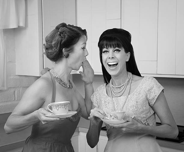 Woman Whispers Joke Caucasian woman whispers joke to friend in her kitchen gossip photos stock pictures, royalty-free photos & images