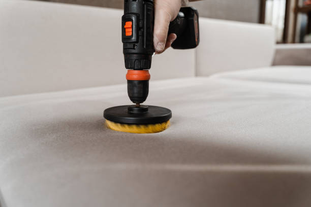 istock Applying detergent on sofa in home interior for dry cleaning. Smearing detergent on couch using drill with brush for dry cleaning. 1494060244