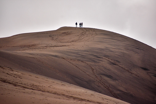 Three hikers climb sand dunes at Great Sand Dunes National Park. Footprints in the sand.