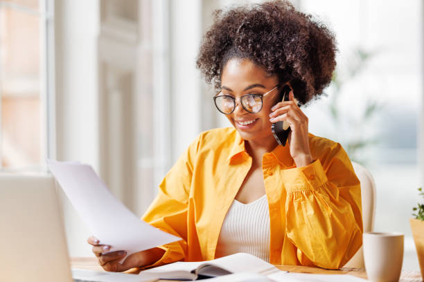 istock Beautiful young smiling ethnic woman making call via smartphone while working remotely from home while sitting at desk and talking to coworkers 1494065632