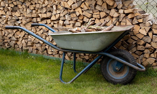 chopped firewood in a woodpile in the country and a wheelbarrow with firewood