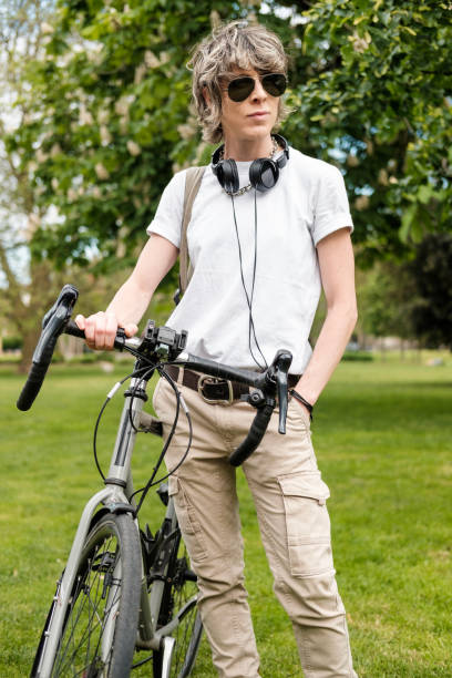 Androgynous person standing with bike in park.