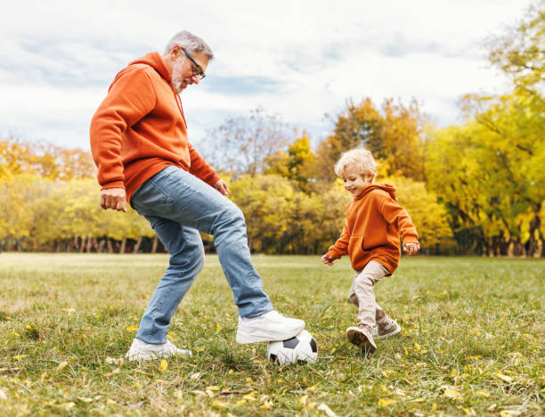 happy family grandfather and grandson play football on lawn in park - avô imagens e fotografias de stock
