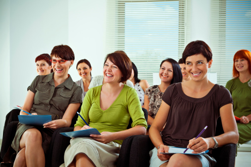 Large group of smiling women listening to a trainer on seminar.