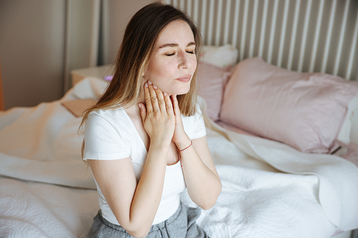 Close up young woman using hand for touching neck with feeling sore throat after wake up in the morning at bedroom , health care lifestyle people concept