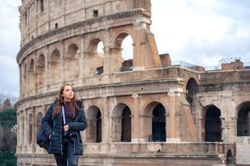 Pensive young Latin woman tourist in Colosseum and looking away while admiring historic architecture during trip through Rome, Italy