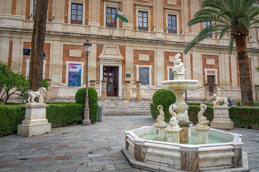 Seville, Spain - Apr 7, 2019: Fountain of the Indies and Sculptures in front of General Archive of the Indies (Archivo General de Indias) - Seville, Andalusia, Spain