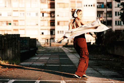 Beautiful young blonde listens to music through headphones and a smartphone and dances in the city