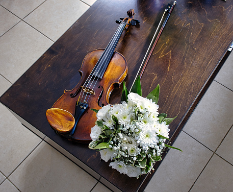 Violin, bow and bouquet of white flowers on a wooden table.