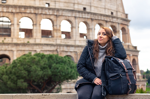 Happy Latin tourist woman in front of historic building Colosseum in Rome, Italy against cloudy sky