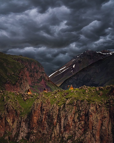 A tent erected on a hill amidst mountainous terrain, with a dramatic backdrop of dramatic and menacing stormy clouds