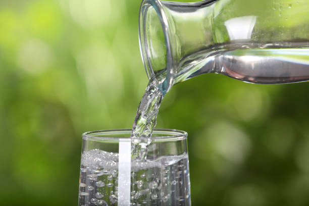 istock Pouring water from bottle into glass on blurred green background, closeup 1494089086