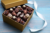 Open box of delicious chocolate candies and color ribbon on light blue wooden table