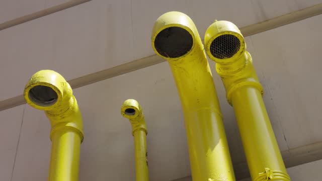 Four strange bright vibrant yellow pipes spill out from teh side of a white concrete building