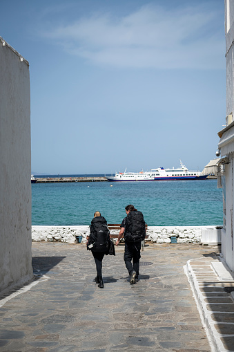 Mykonos, Greece - May 14, 2023: Two backpackers walk toward the port in Mykonos town.
