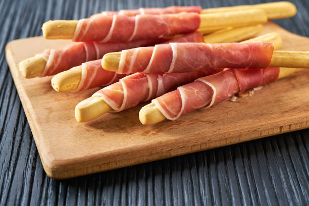 Parma ham prosciutto with Italian grissini breadsticks on a black wooden table . stock photo