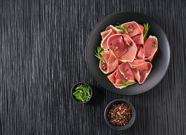 Spanish jamon cut, parma ham cutting with rosemary and spice on a black wooden table, top view. stock photo