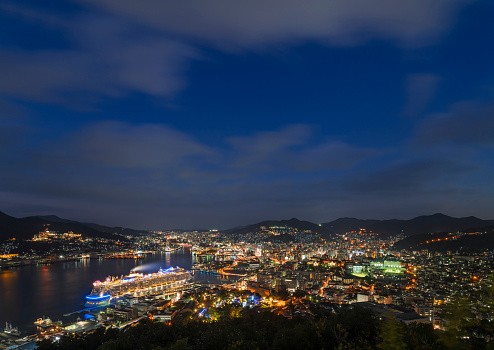 Bird's-eye view at night from Mt Nabekanmuri of cruise ship moored at International Terminal with the city port Nagasaki bay surrounded by mountains.