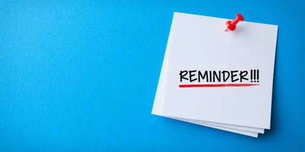 Photo of White Sticky Note With Reminder And Red Push Pin On Blue Background