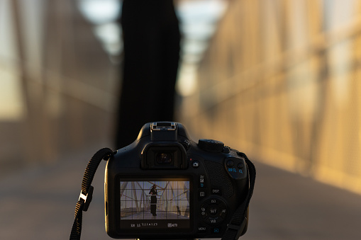 image of a young girl dancing on a pedestrian bridge and filming herself with a professional camera on a tripod on the ground. View from camera screen