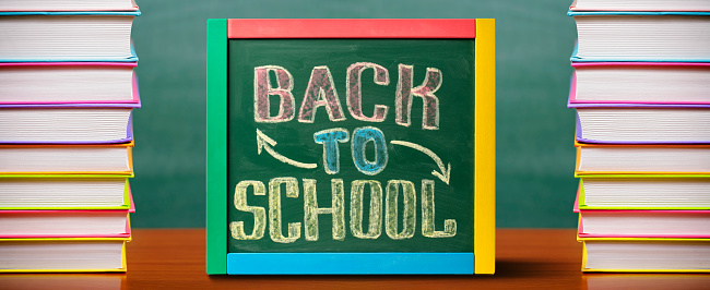 Chalkboard with BACK TO SCHOOL lettering hand drawn by colorful chalk. Stacks of books at the background.