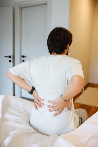 istock Young man sitting on bed and suffering from back pain stock 1494097506