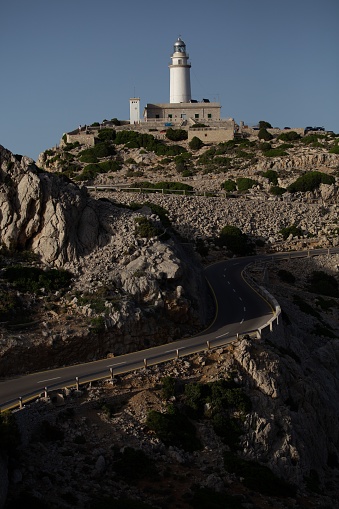 This image is of a white lighthouse perched atop a mountain surrounded by rocky terrain and rolling hills