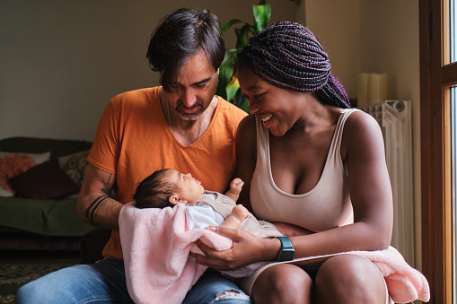 Portrait of a multiethnic couple with a newborn in arms at home