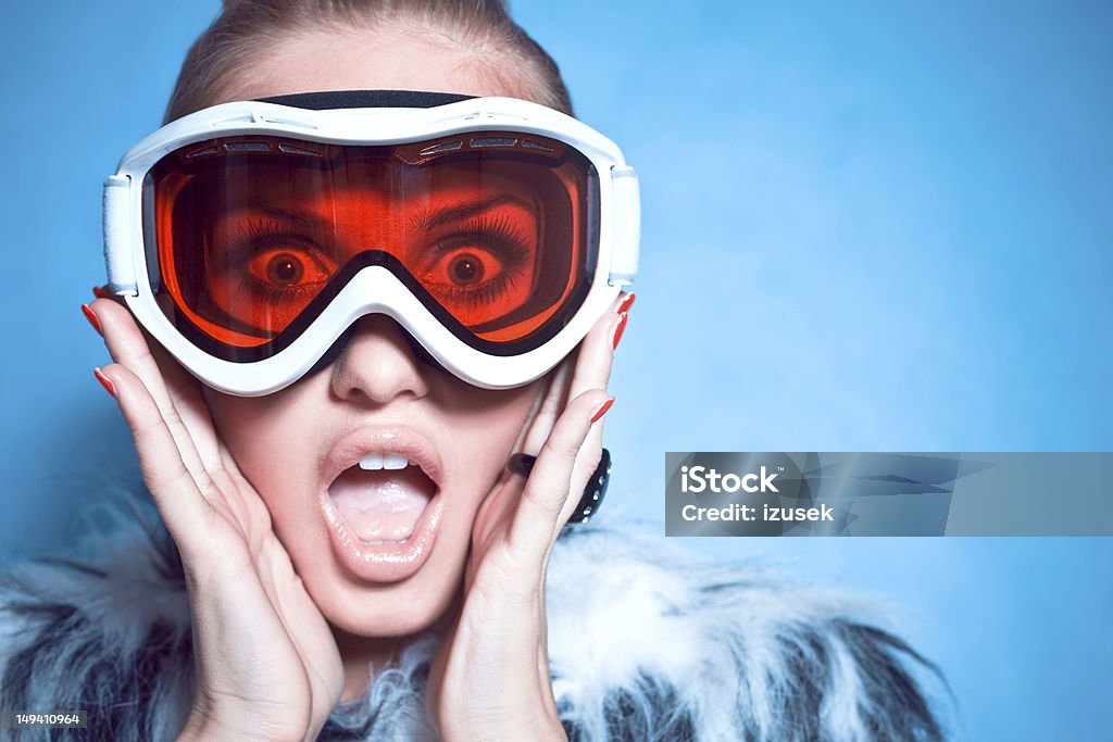 Screaming Winter Girl Winter portrait of a stylish young woman wearing fur coat and goggles, looking at camera and screaming. Studio shot. Snow Stock Photo