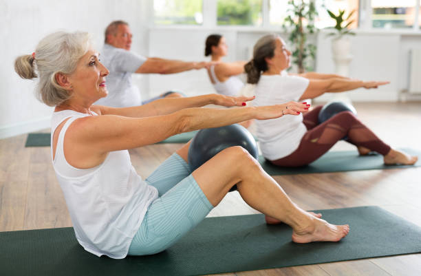 Portrait of elderly people doing exercises for press with pilates ball during group class in fitness studio stock photo