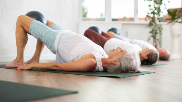 gruppe älterer menschen, die pilates auf matte im studio machen - senior adult exercising aging process instructor stock-fotos und bilder