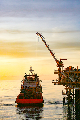 A striking image of an offshore oil rig at sunset off the coast of Huntington Beach, California. The pink & orange tones of the setting sun highlight the industrial machinery and equipment used in the drilling and extraction of fossil fuels, including crude oil and natural gas. \n\nThe scene captures the intersection of the energy industry and the beauty of the Pacific Ocean. The image speaks to issues of fuel and power generation, energy crises, and environmental concerns surrounding the oil and gas industry.