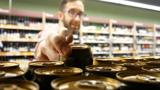 Close-up of many beer cans on a store shelf and a smiling bearded man with glasses taking one stock photo
